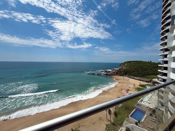 Une vue sur la plage depuis un balcon, avec une piscine et un immeuble doté de balcons.