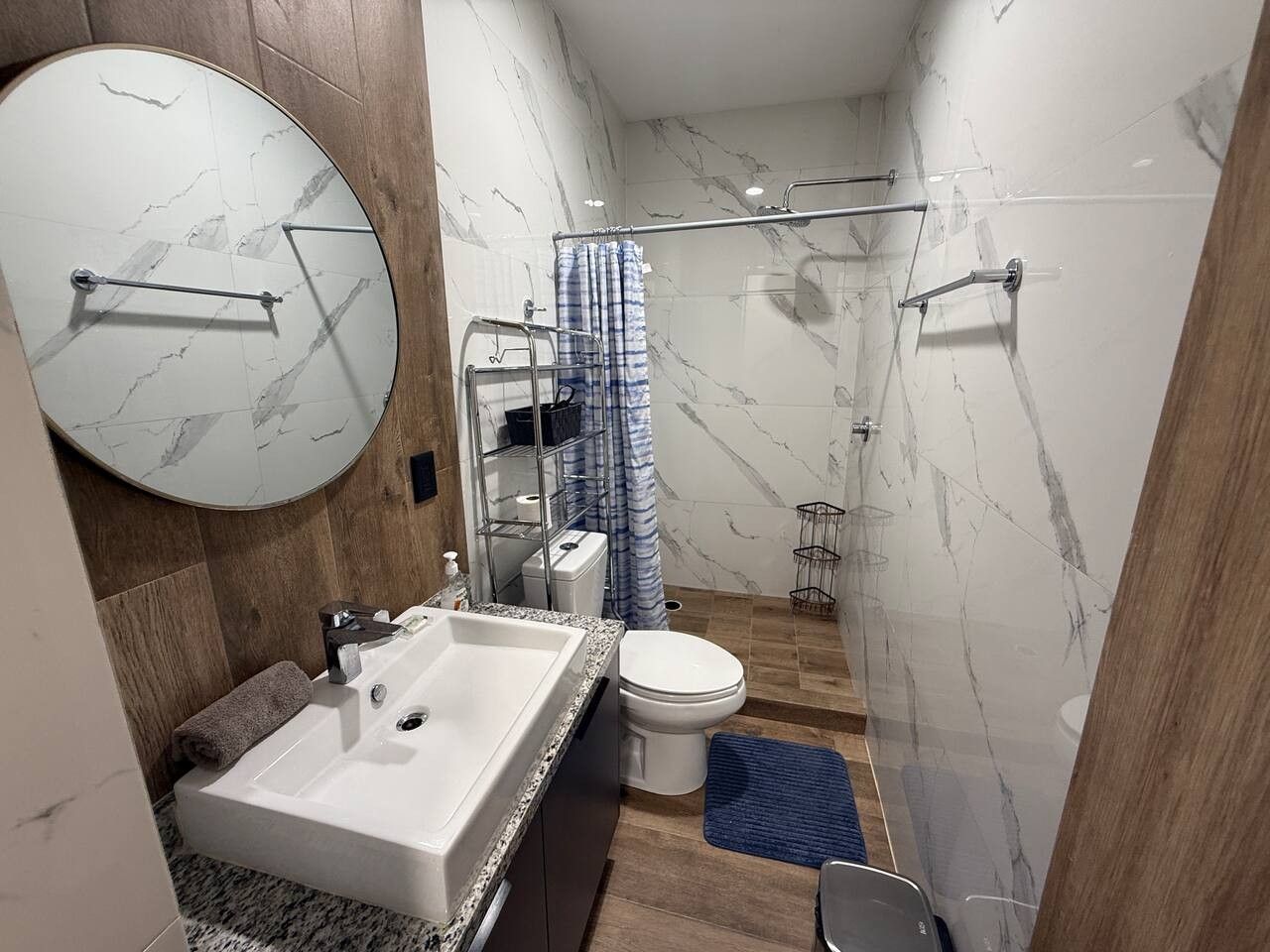 Uma casa de banho moderna com parede de mármore, lavatório, sanita e zona de duche.