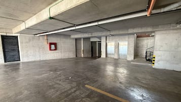 Un grand parking souterrain vide, avec des planchers et des murs en béton, des poutres apparentes et un extincteur fixé au mur.