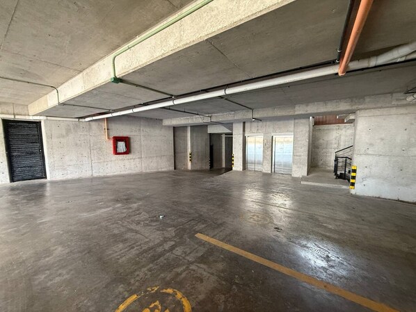 A large, empty parking garage with concrete floors and walls, visible structural beams, and a fire extinguisher mounted on the wall.