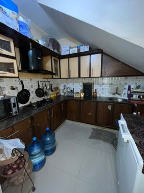 Cocina con armarios de madera, microondas, estufa y lavamanos. Hay jarras de agua y un radiador blanco.