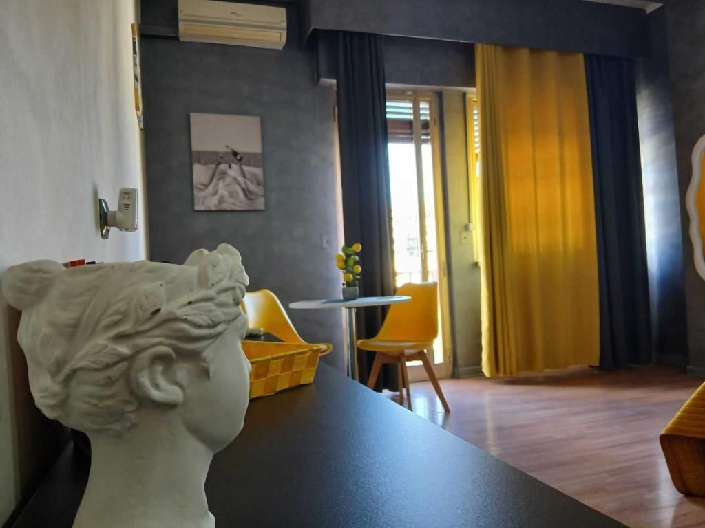 Een kamer met een marmeren borstbeeld, een eettafel met stoelen, een bijzettafeltje met bloemen en een uitzicht op het omliggende landschap door een deuropening.