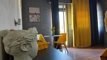 Een kamer met een marmeren borstbeeld, een eettafel met stoelen, een bijzettafeltje met bloemen en een uitzicht op het omliggende landschap door een deuropening.