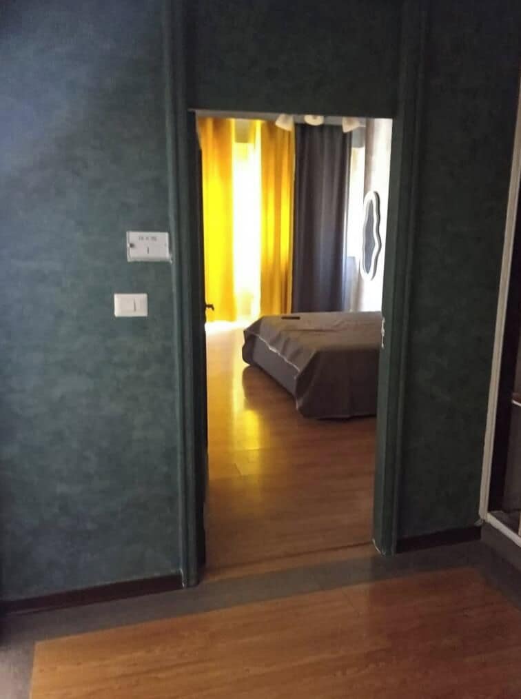 A room with a bed, a window with curtains, and a door leading to another room.