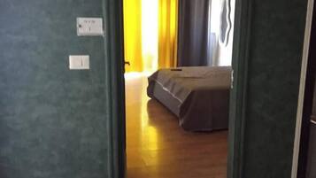 A room with a bed, a window with curtains, and a door leading to another room.
