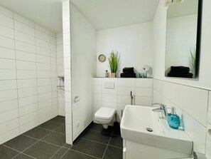 A bathroom with a white sink, a toilet, a shower area, and a mirror. - Beachcomber F3norderney (Norderney)