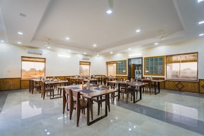 Un vaste espace dédié à la salle à manger, comprenant plusieurs tables et chaises, des unités de climatisation et de grandes fenêtres offrant une vue dégagée.