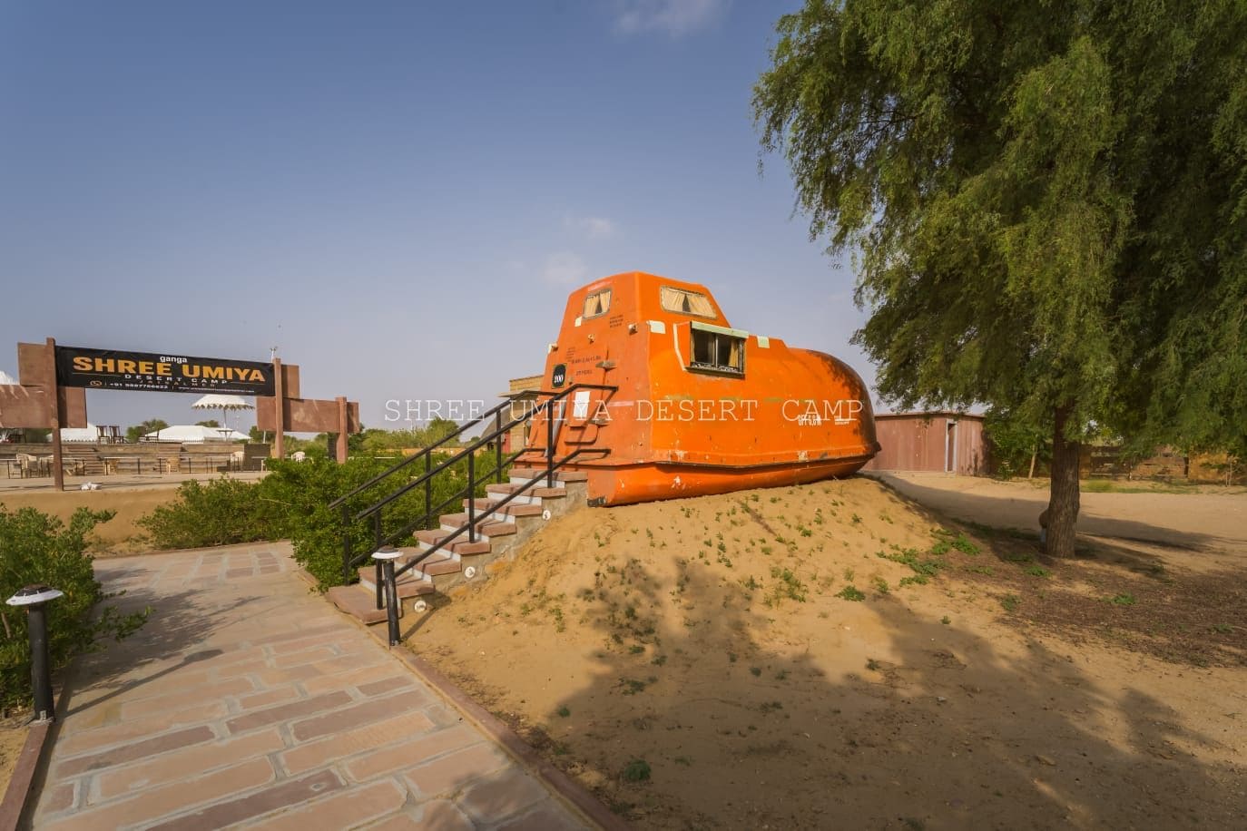 Un campement dans le désert, avec un bâtiment orange qui se distingue, un escalier menant à celui-ci et un panneau indicateur.
