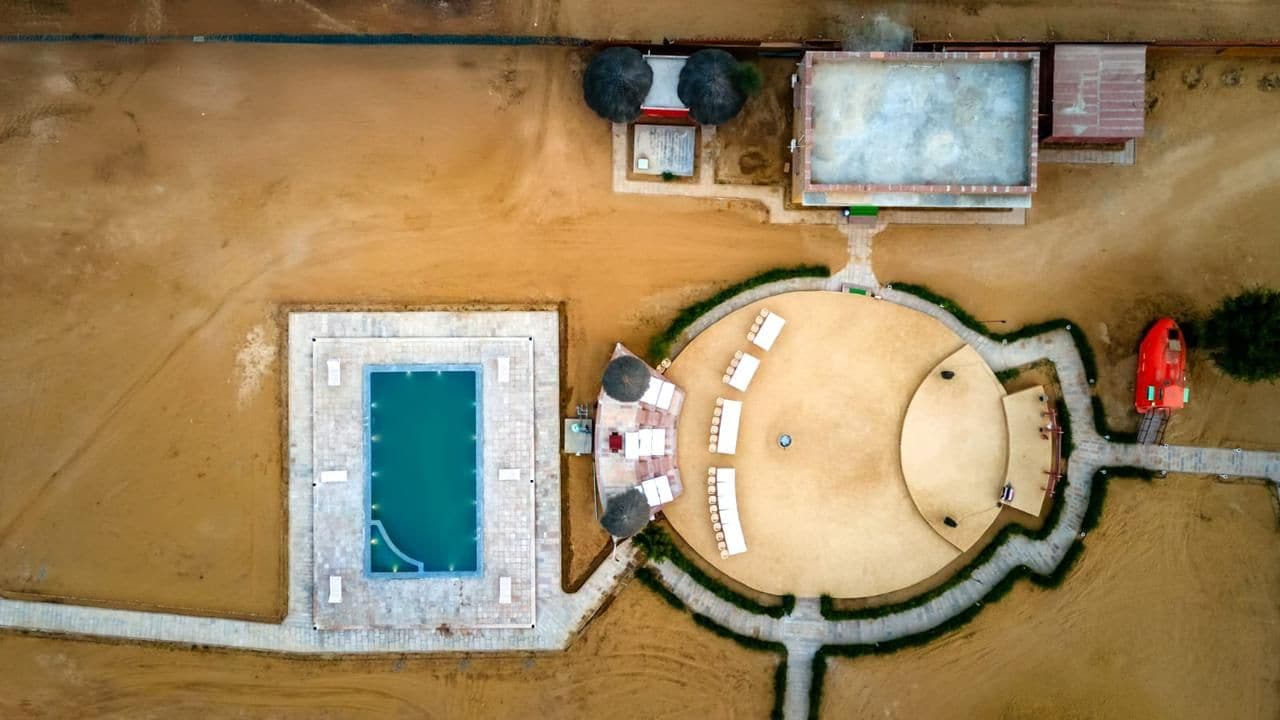 Vista aérea de una propiedad con piscina, zona de estar circular al aire libre y piscina rectangular.