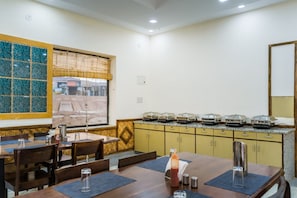 Un comedor con mesas y sillas de madera, una barra de buffet con platos cubiertos y una pared decorativa con un motivo geométrico.