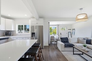 A modern kitchen with a large island, a dining area with a table and chairs, and a living room with a sofa and a coffee table. - Modern 4BR Home - Parking - Close to Downtown (Seattle)
