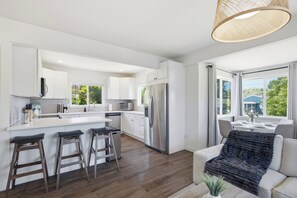 A modern kitchen with white cabinets, a stainless steel refrigerator, and a large island with bar stools. - Modern 4BR Home - Parking - Close to Downtown (Seattle)