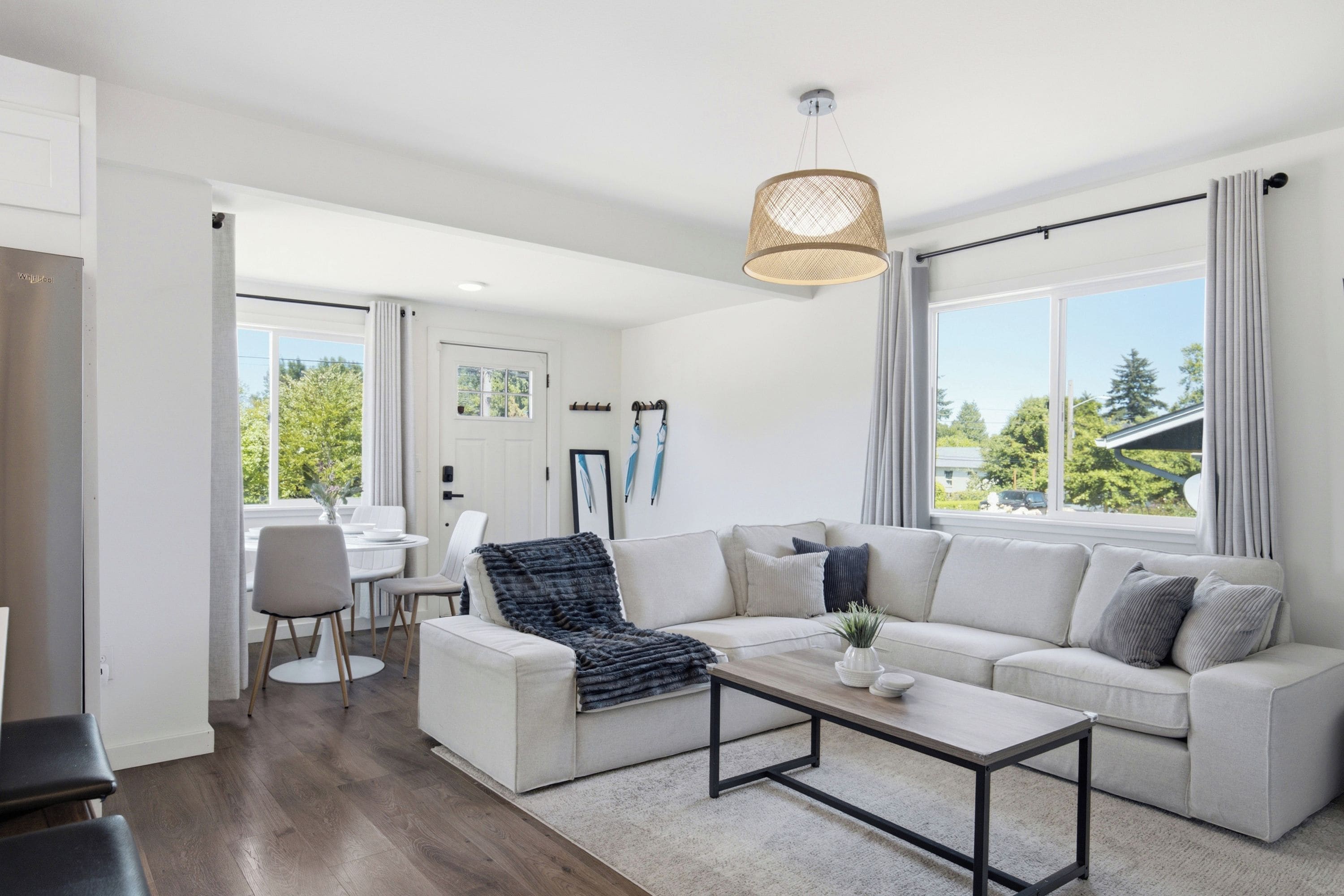 A modern living room with a white sofa, a coffee table, and a dining area with a white table and chairs.