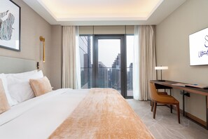 Quarto de hotel com uma cama grande, uma escrivaninha, uma cadeira, vista para a cidade e uma moldura na parede.
