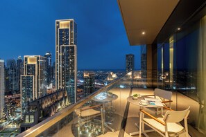A high-rise building with a balcony featuring a table and chairs, overlooking a cityscape at night. - bnbme - Address Opera Tower 1 - 2BR (Dubai)