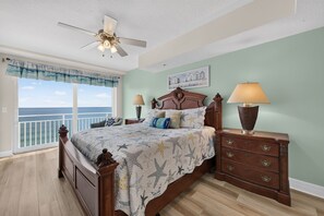 A bedroom with a large bed, a nightstand with a lamp, a dresser, and a ceiling fan. - Serenity at The Opus (Daytona Beach)
