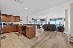 A spacious kitchen with wooden cabinets and a dishwasher, leading to a dining area with a large window overlooking the ocean. - Serenity at The Opus (Daytona Beach)