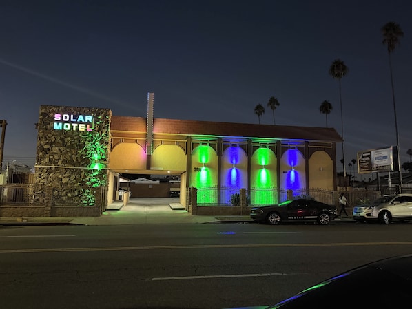 Un motel con letrero de neón, fachada de piedra y entrada con portón.