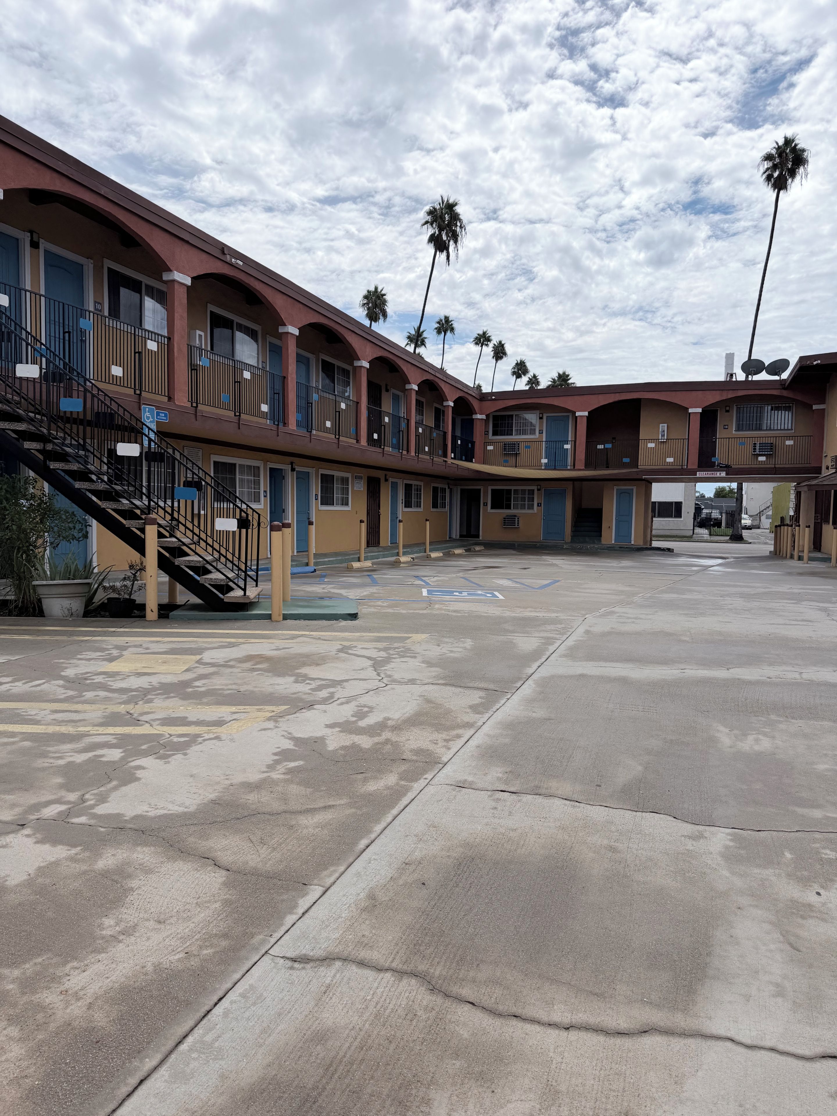 A motel with multiple floors, outdoor parking, and palm trees.
