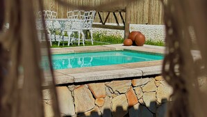 Area piscina con parete in pietra, sedia in metallo bianco e recinzione in legno.