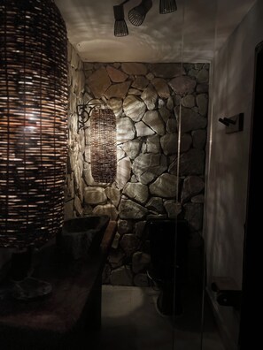 Ein Badezimmer mit einer Steinwand, einer gewobenen Leuchte und einem modernen Waschbecken.