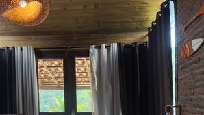 Camera da letto con un letto, tende, una lampada a sospensione e vista sul verde circostante.