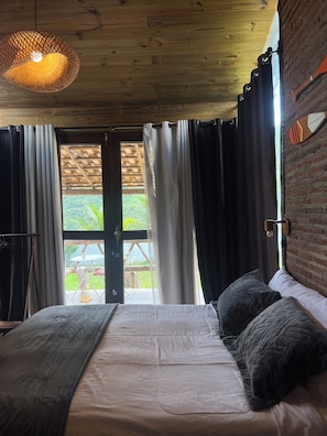 Ein Schlafzimmer mit Bett, Vorhängen, einer Hängelampe und Blick auf Grünfläche.