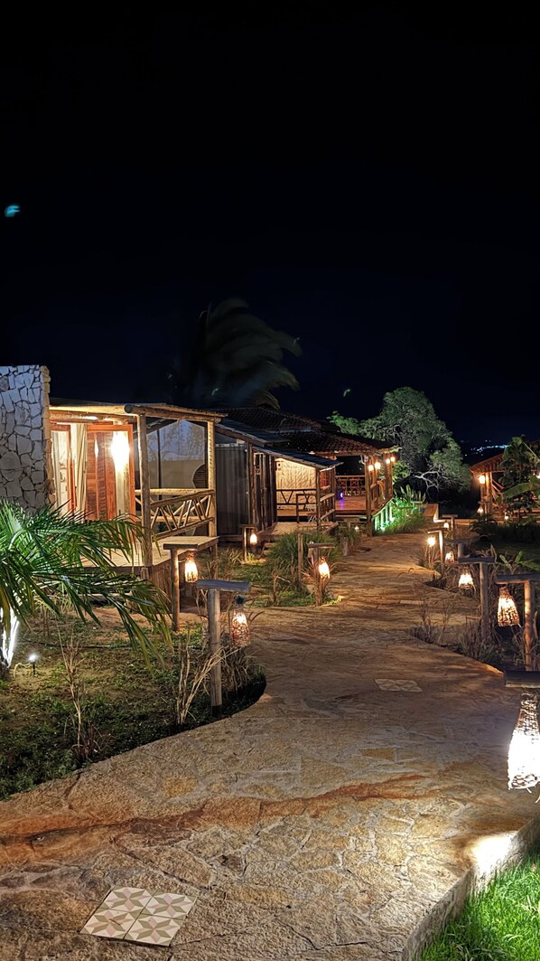 A pathway leading to a rustic building with a stone facade, wooden deck, and ambient lighting.