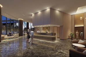 Un hall d’hôtel moderne avec un comptoir d’accueil, des espaces de détente et un grand mur de verre.