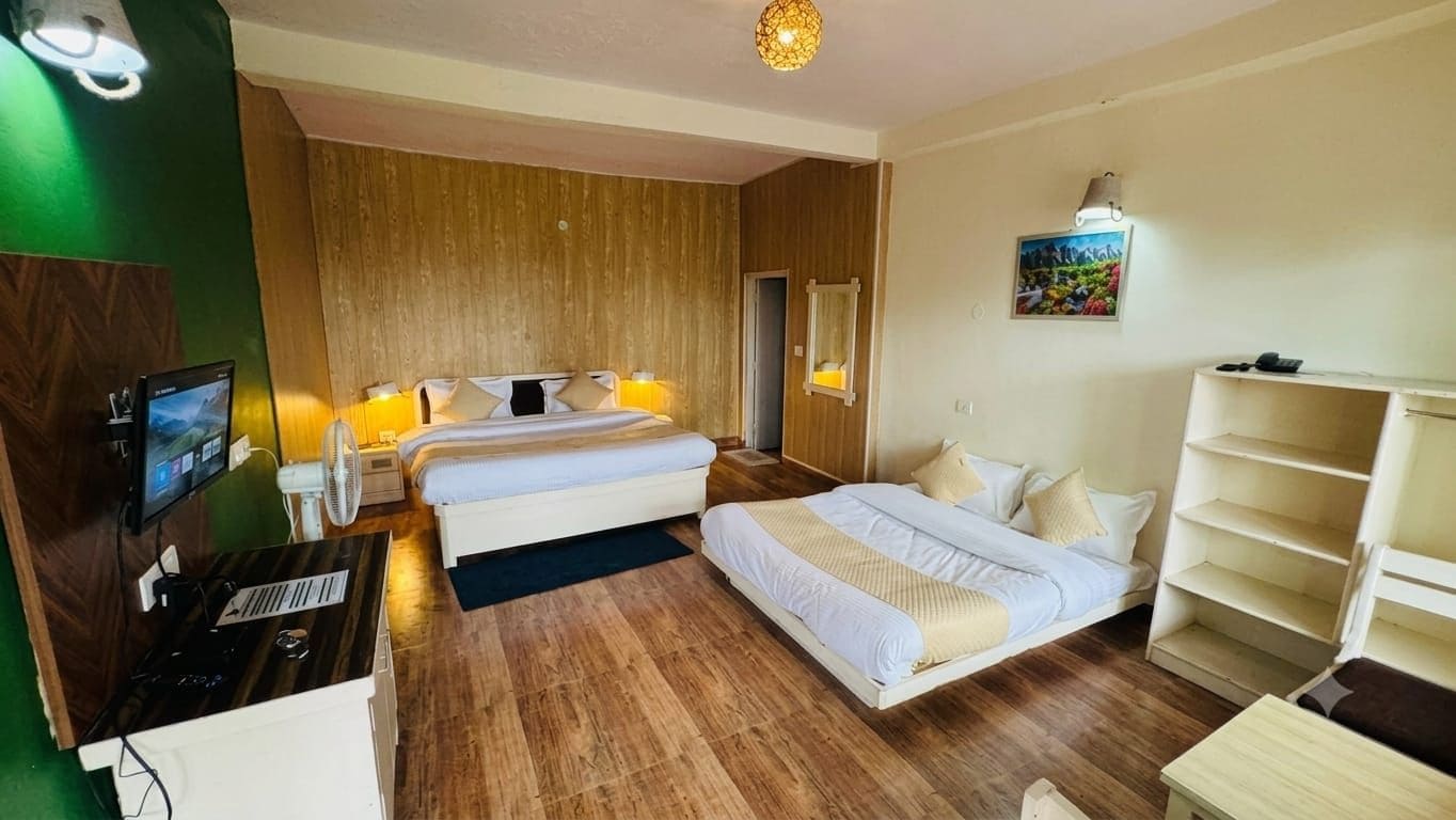 A hotel room with a bed, a desk with a computer, a TV, and a bookshelf.