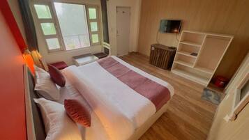 Habitación de hotel con cama, televisor, aparador de madera y ventana con vistas.
