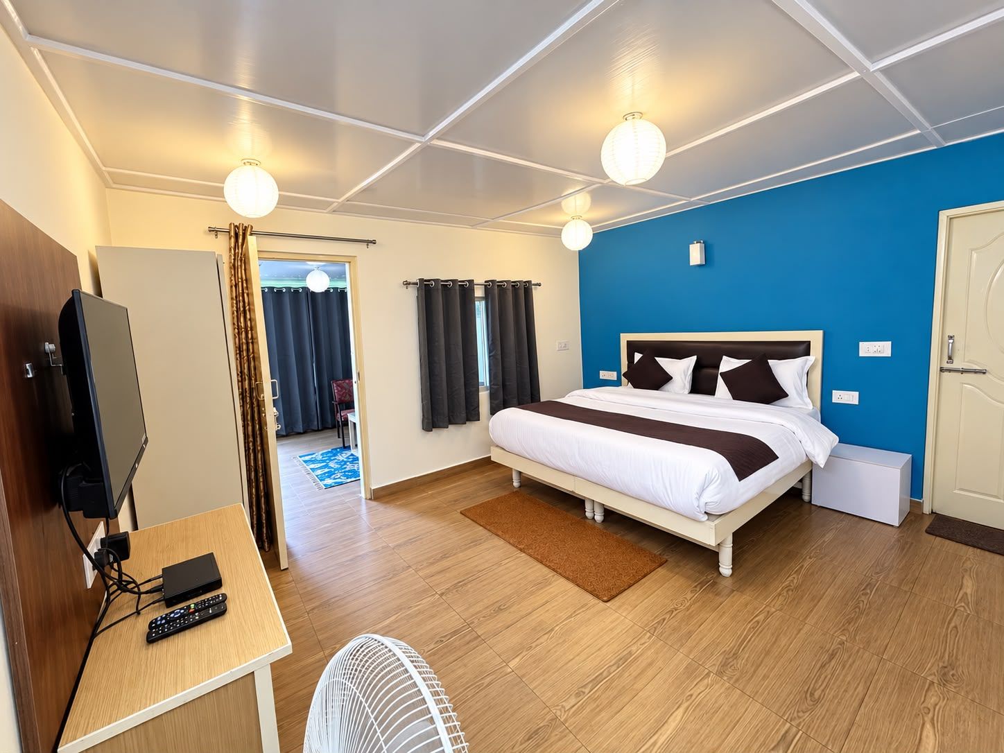 Habitación de hotel con cama, mesita de noche, televisor y ventilador.
