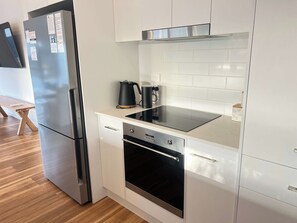 A modern kitchen with a stainless steel refrigerator, a built-in oven, and a black induction cooktop. - The Sandbar - Wi-Fi - No Pets (Robe)