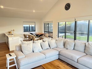 A modern living room with a sectional sofa, a dining table with chairs, and a kitchen area with a sink and cabinets. - The Sandbar - Wi-Fi - No Pets (Robe)