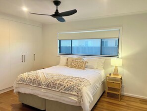 A bedroom with a bed, a ceiling fan, a window with blinds, a bedside table with a lamp, and a wardrobe. - The Sandbar - Wi-Fi - No Pets (Robe)