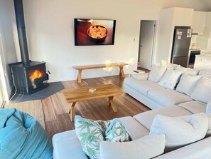 A modern living room with a wood-burning stove, a sofa set, a coffee table, and a television mounted on the wall. - The Sandbar - Wi-Fi - No Pets (Robe)