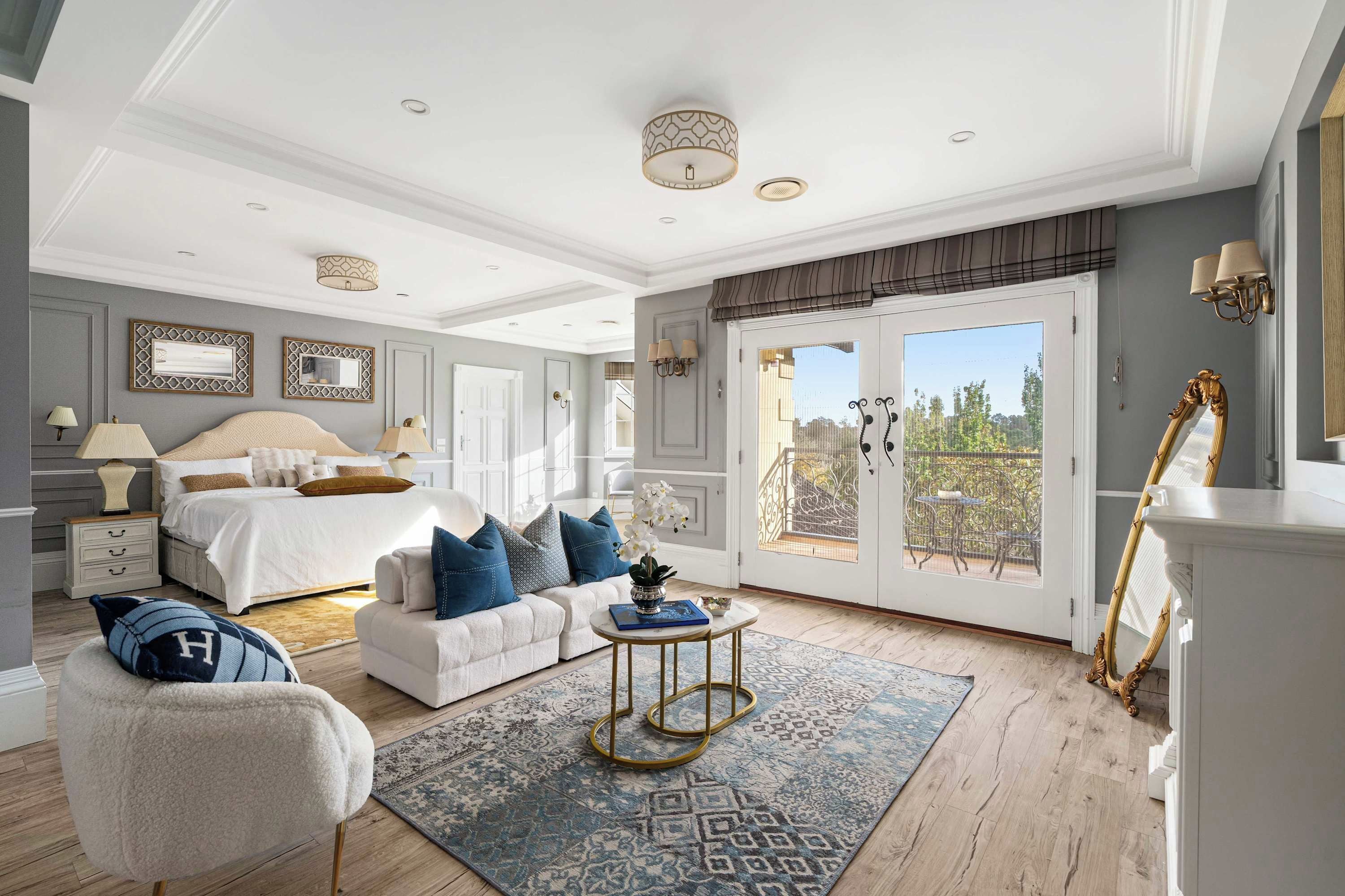 Une chambre spacieuse avec un grand lit, un coin salon comprenant un canapé et un fauteuil, une petite table ronde et un balcon aménagé avec du mobilier d’extérieur.