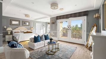 Une chambre spacieuse avec un grand lit, un coin salon comprenant un canapé et un fauteuil, une petite table ronde et un balcon aménagé avec du mobilier d’extérieur.