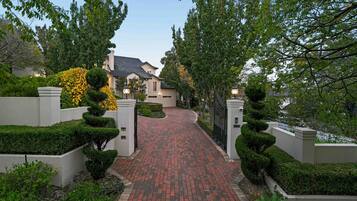 A residential driveway leading to a house with a brick pathway, surrounded by well-maintained hedges and trees.
