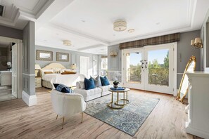 Un espacioso dormitorio con una cama grande, una zona de estar con una silla, una mesita pequeña y vistas a través de una puerta de cristal.