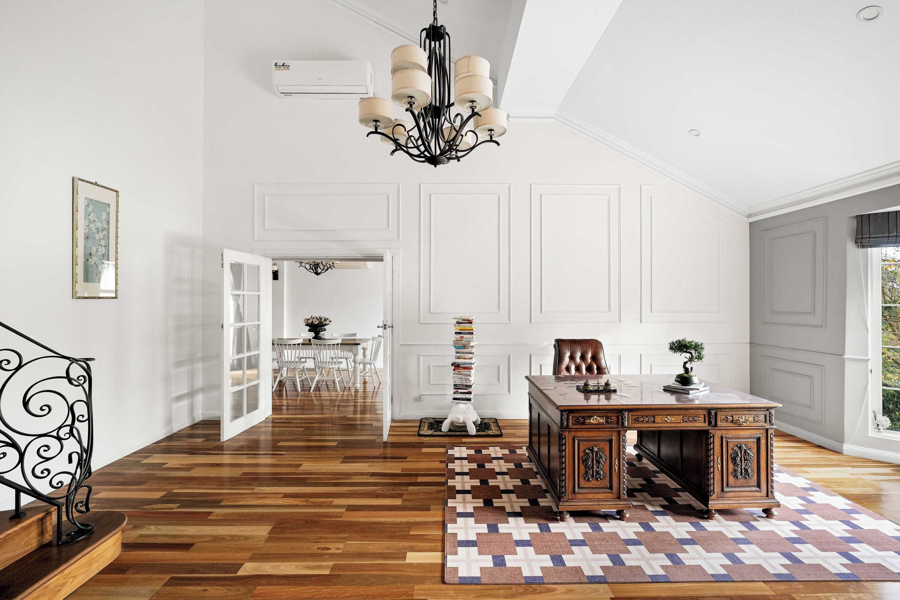 A spacious room with a wooden floor, a desk with a plant, a chandelier, and a view of the outdoors.