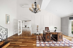 A spacious room with a wooden floor, a desk with a plant, a chandelier, and a view of the outdoors.