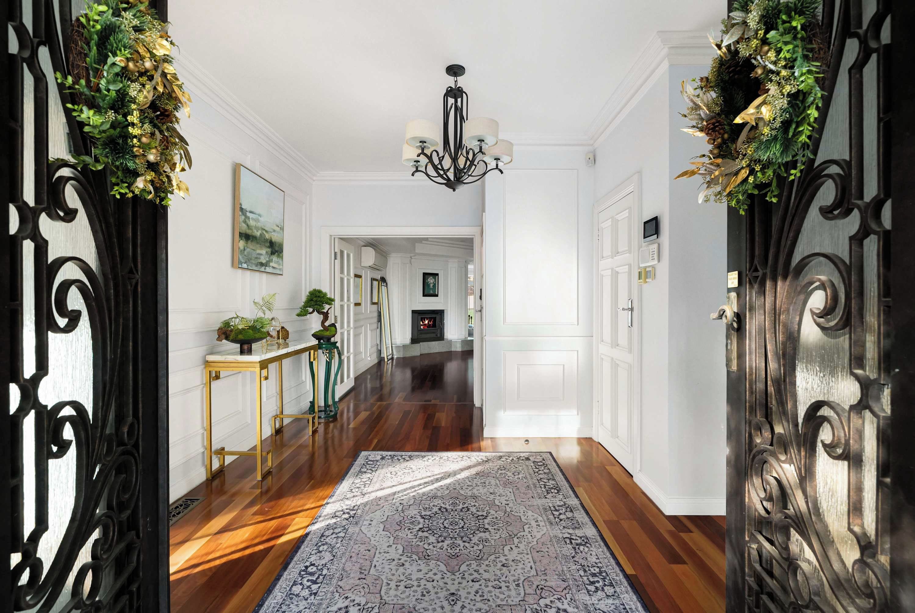 A hallway with a patterned rug, a chandelier, and a fireplace in the background.