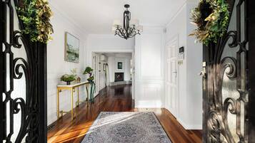 A hallway with a patterned rug, a chandelier, and a fireplace in the background.