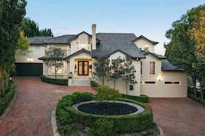 A two-story house with a brick driveway and a landscaped front yard.