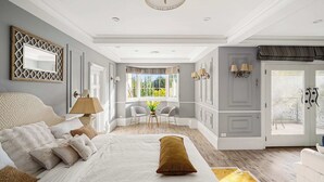 Quarto com uma cama grande, área de estar com cadeiras, janela com cortinas e porta com cortina.