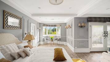 Une chambre à coucher avec un grand lit, un coin salon avec des fauteuils, une fenêtre avec des rideaux et une porte également dotée d’un rideau.