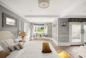 Une chambre à coucher avec un grand lit, un coin salon avec des fauteuils, une fenêtre avec des rideaux et une porte également dotée d’un rideau.