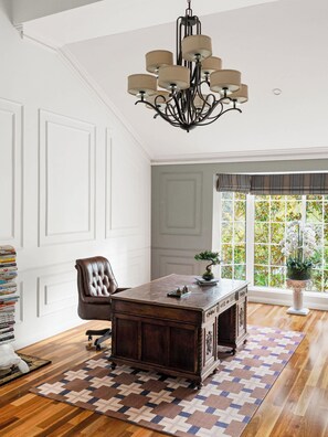 Una habitación con escritorio de madera, sillón de cuero, candelabro y ventana con vista a la vegetación.