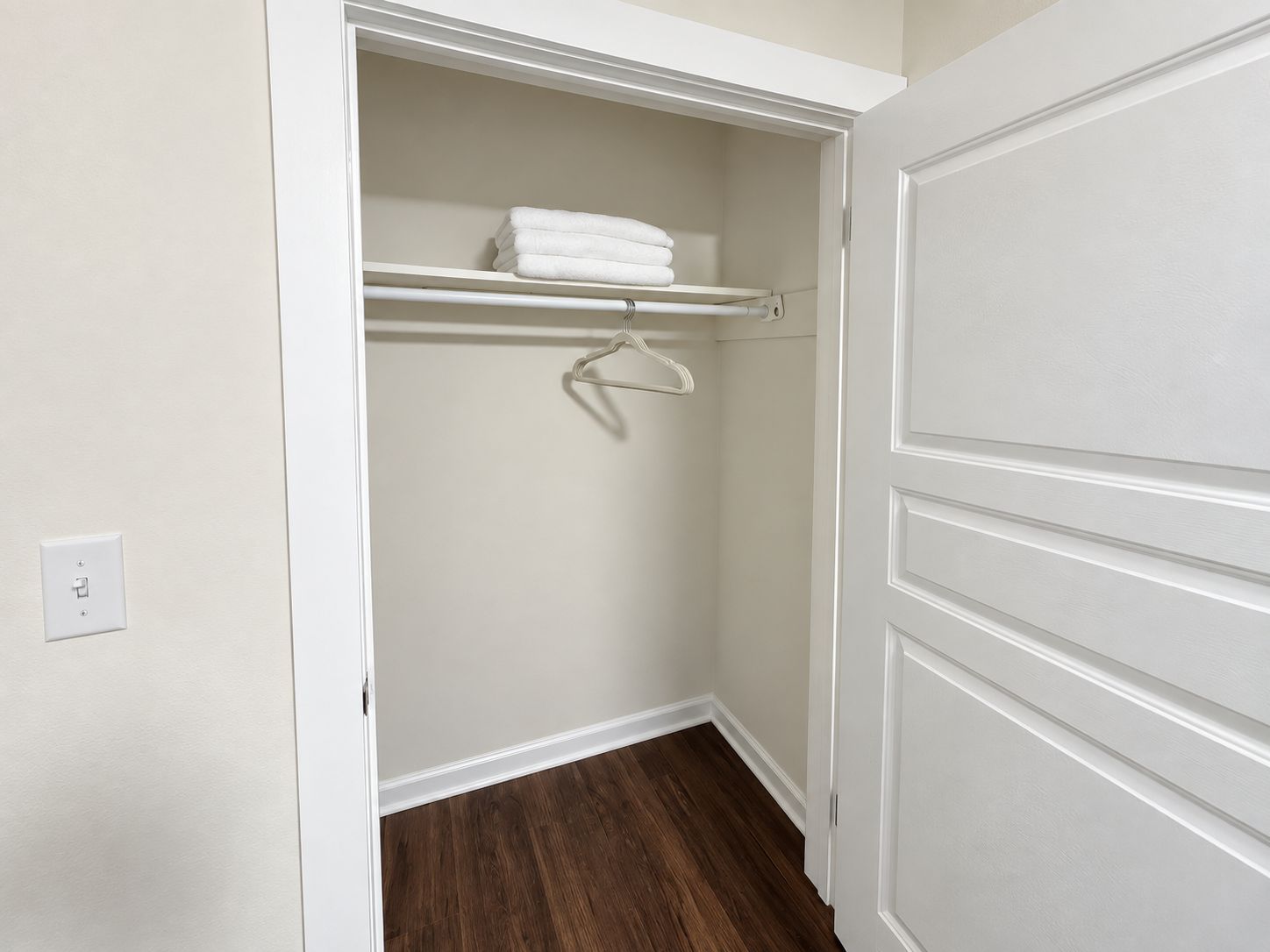 A walk-in closet with a wooden floor, a white door, and a shelf with folded towels.